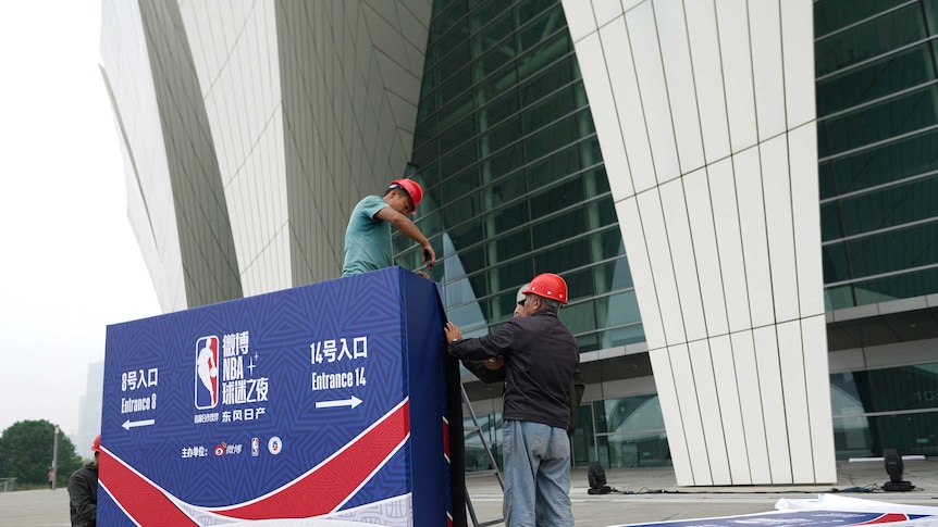 Two workmen in hard hats drilling a sign with NBA basketball signage