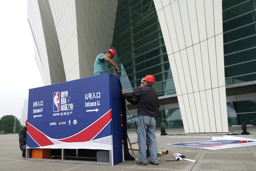 Two workmen in hard hats drilling a sign with NBA basketball signage