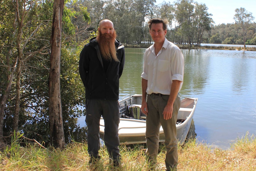 Ecologists Peter Goonan and Matt Bell standing in front of boat on riverbank of Wallace Lake Catchment.