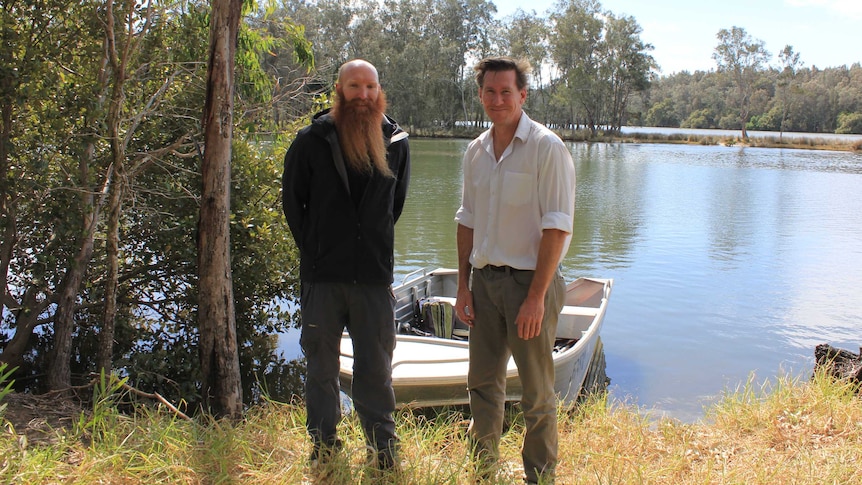 Ecologists Peter Goonan and Matt Bell standing in front of boat on riverbank of Wallace Lake Catchment.