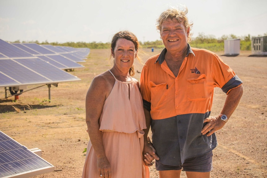 Lyn and Doug Scouller smiling at the camera, in front of solar panels on their Queensland property.