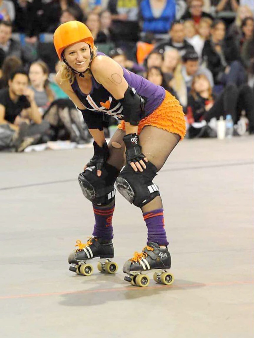 A woman wearing roller skates and protective clothes rests in front of a crowd