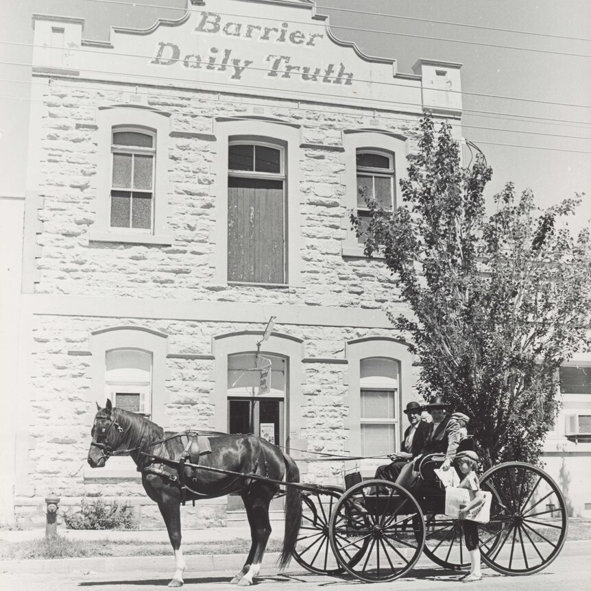 A horse and cart collecting a newspaper from a child at the front of a building.
