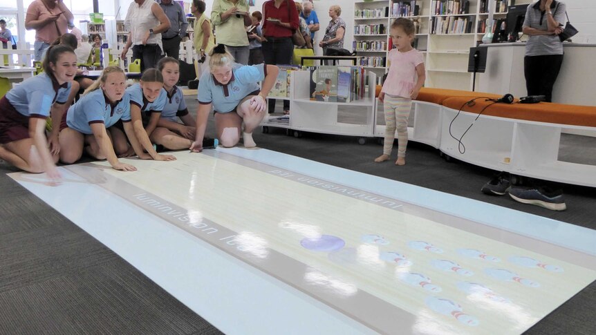 School children play a game of ten-pin bowling on the floor, as part of a new interactive instalment in a library.