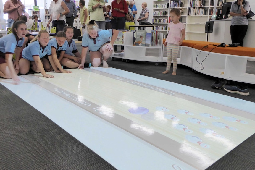 School children play a game of ten-pin bowling on the floor, as part of a new interactive instalment in a library.