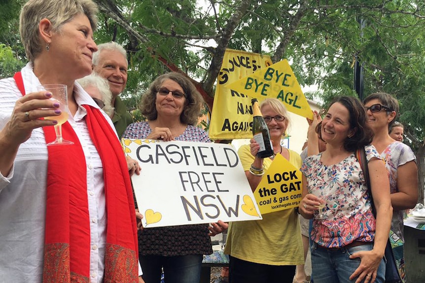 A group of people hold champagne and signs with messages such as 'Bye Bye AGL' and 'Gasfield Free NSW'