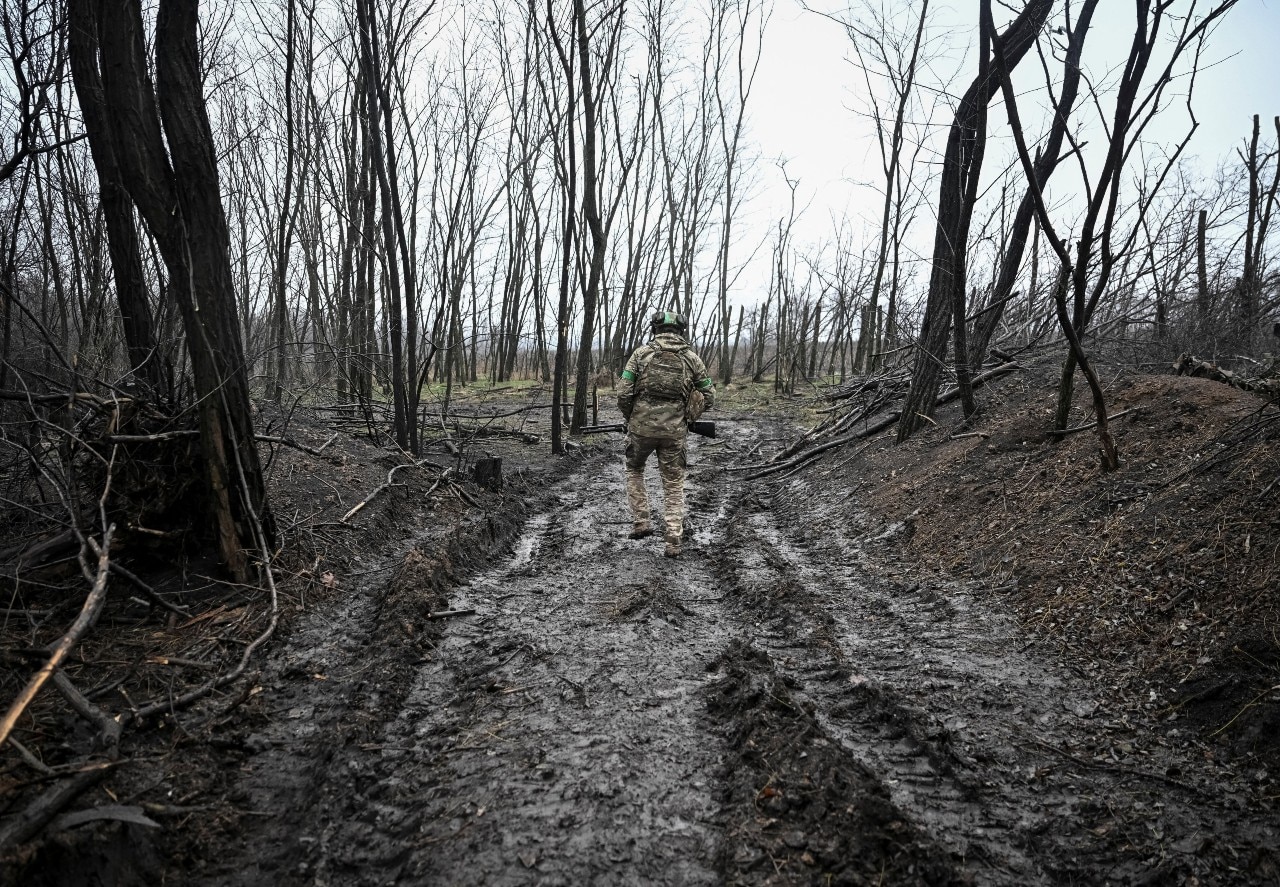 A soldier walking on a muddy track through trees, seen from behind