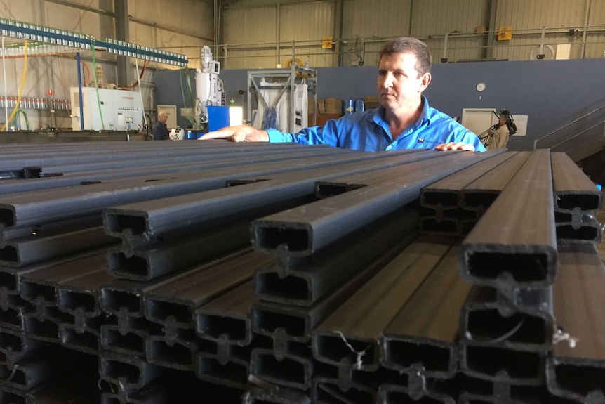 A man in a blue shirt looks at a large pile of fence palings.