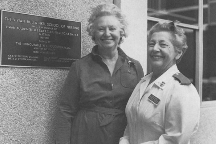 Vivan Bullwinkel and Shirley Boden smile as they stand beside a plaque outside the dedicated nursing ward in a photo.
