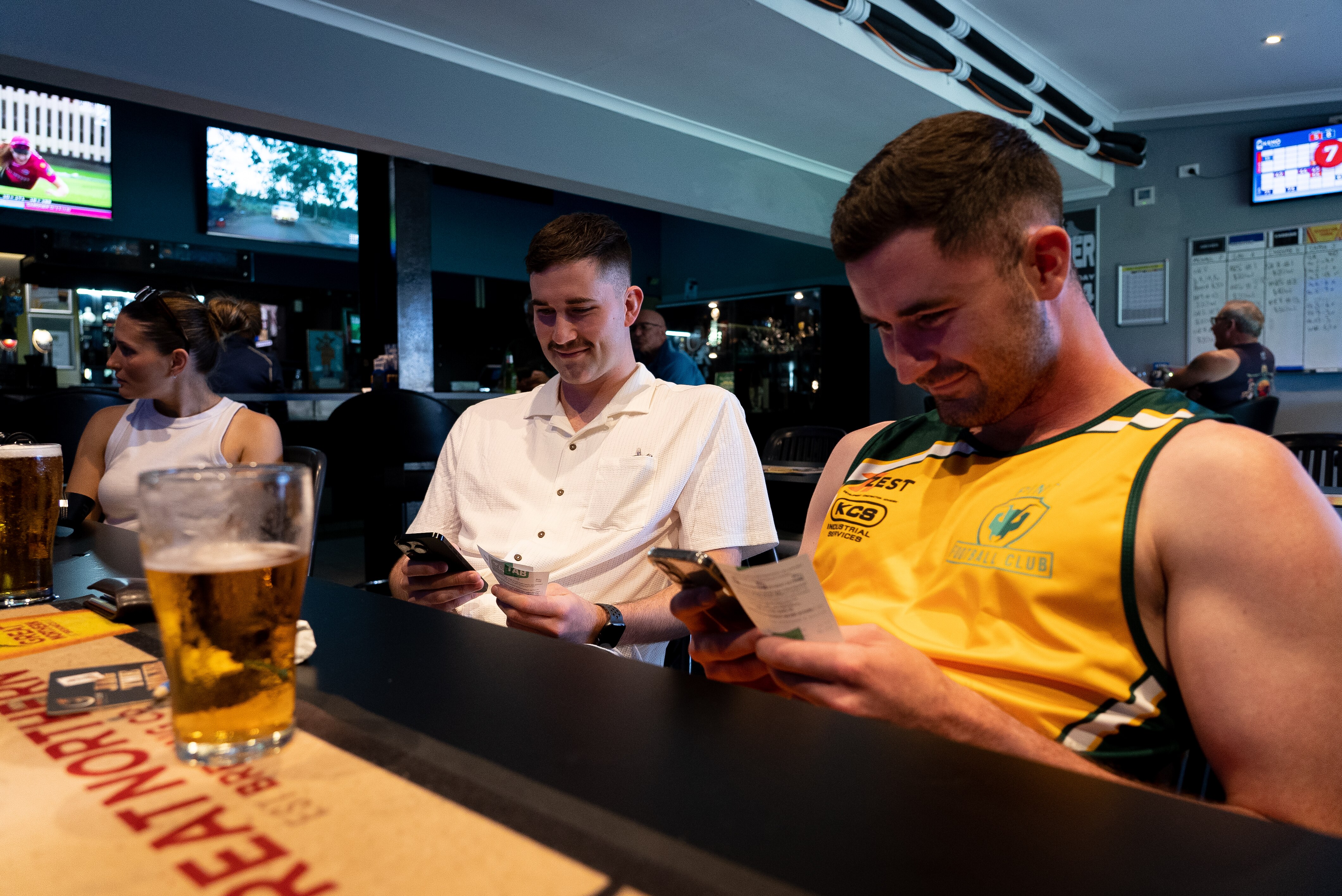 Two men sit in a bar with a beer looking at their phones