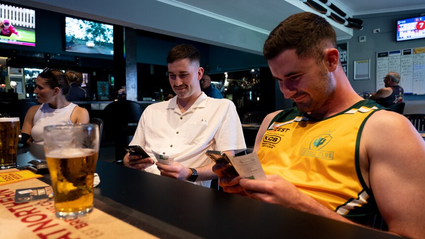 Two men sit in a bar with a beer looking at their phones