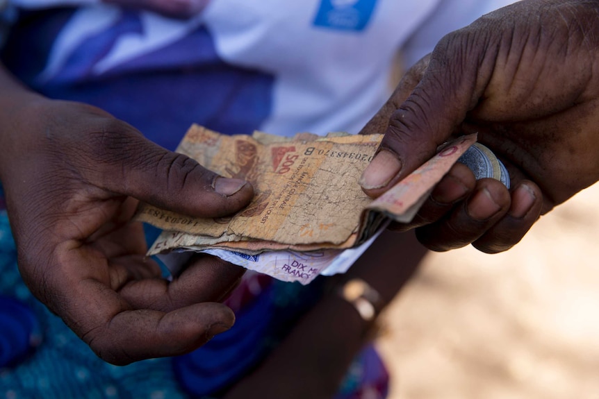 Money party of a microfinance loan changes hands in front of blue fabric in the background.