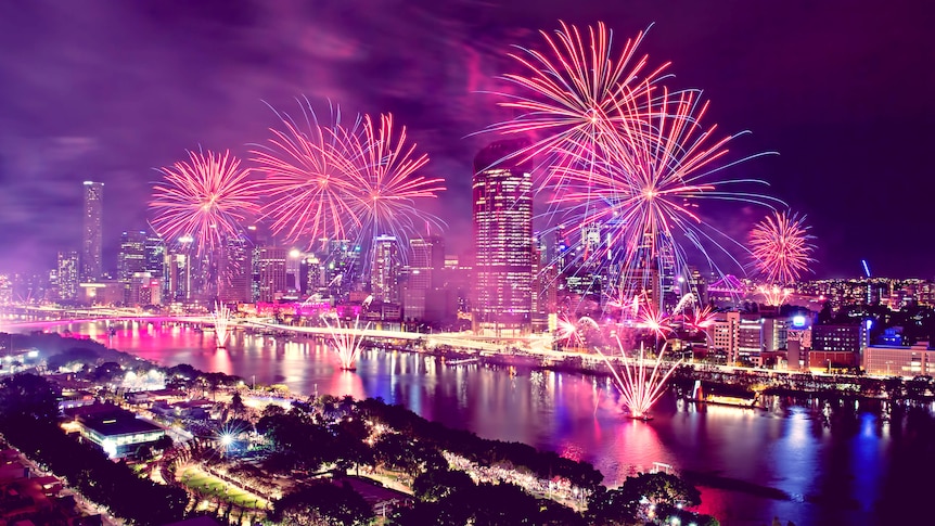 The Brisbane River and skyline at night illuminated by a fireworks display.