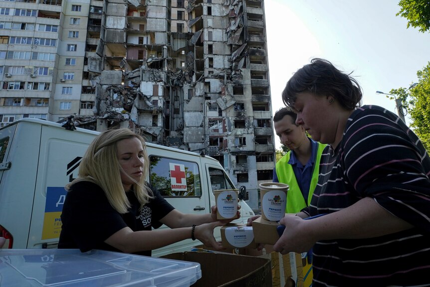 Local residents get free meals from volunteers against the background of their damaged apartment house.