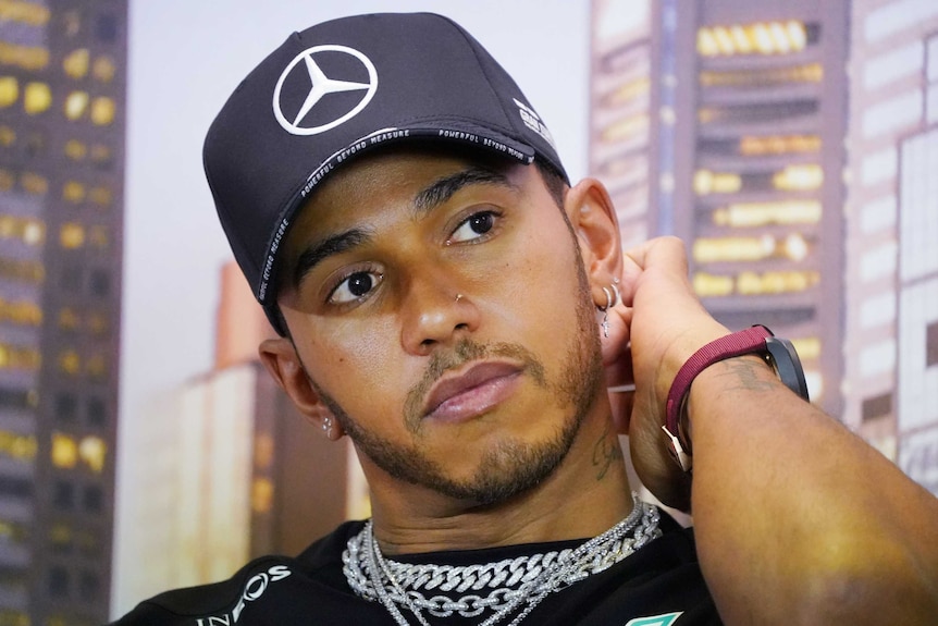 A male Formula One driver holds his neck as prepares to answer a question ahead of the Australian Grand Prix in Melbourne.