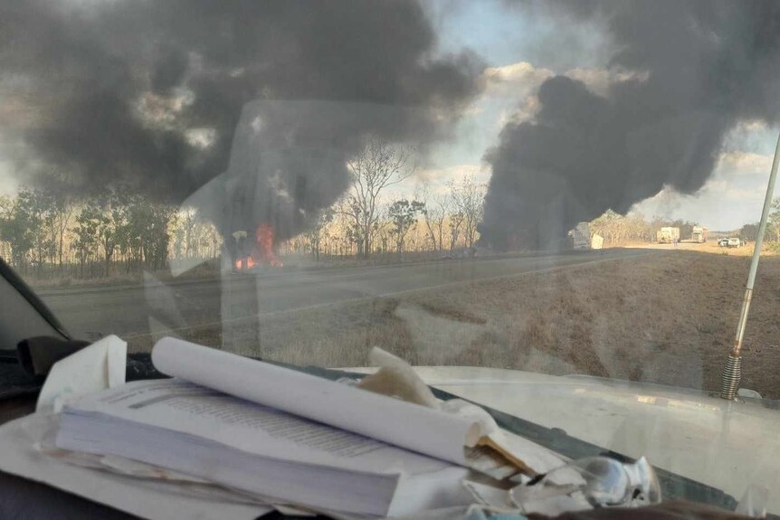 Picture of car crash from inside another car parked across the road, with fire and smoke visible from the crash site