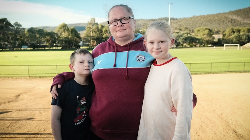 A woman with glasses stands in between a young boy and young girl