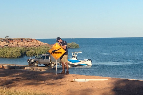A Broome Shire Council ranger erects a crocodile warning sign at Town Beach.