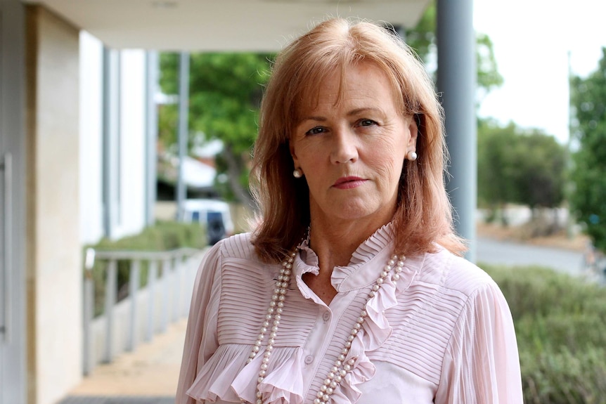 Head shot of a woman with auburn hair wearing pearls.