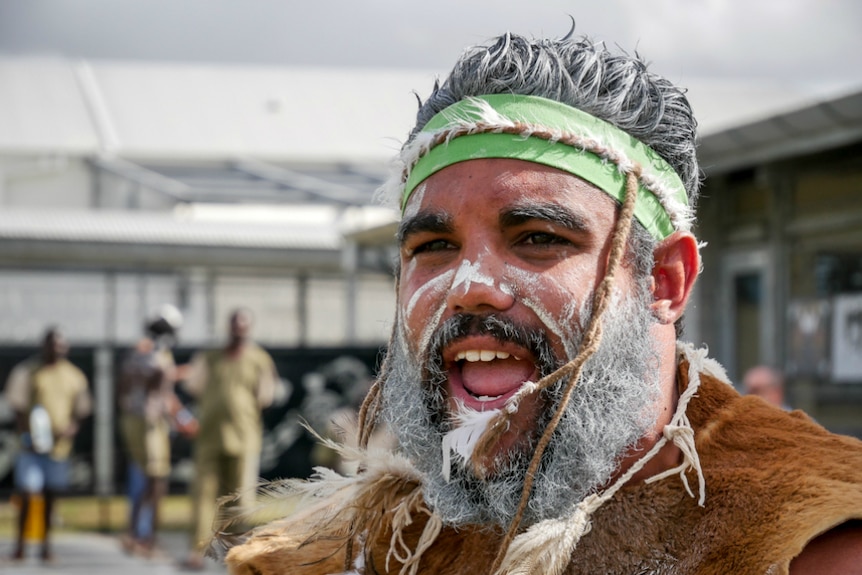 A close-up of a male Indigenous performing, with white-painted hair and beard.