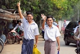 Reuters reporters Wa Lone and Kyaw Soe Oo wave to cameras as they walk down a dirt road carrying bright yellow and blue bags.