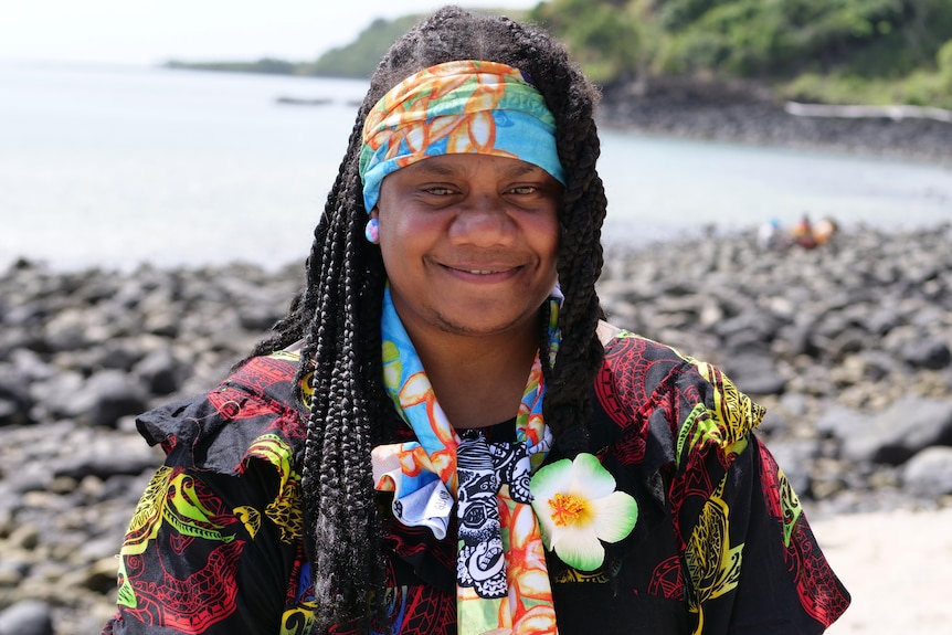 woman with floral headband and colourful dress, wearing flower on dress smiling at the camera.10-++-