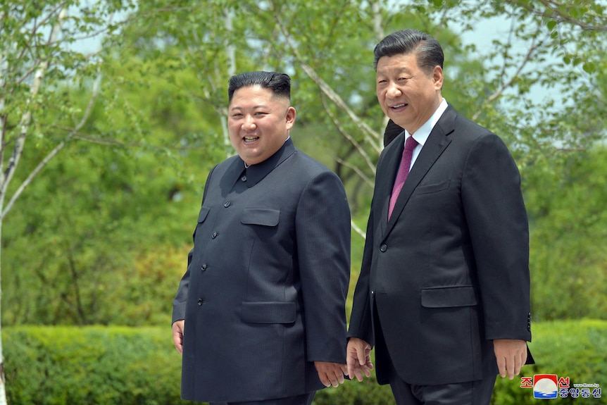 Kim Jong Un stands next to Xi Jinping with greenery behind them.