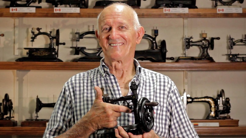 Les Walsh stands in front of a shelf of vintage sewing machines.