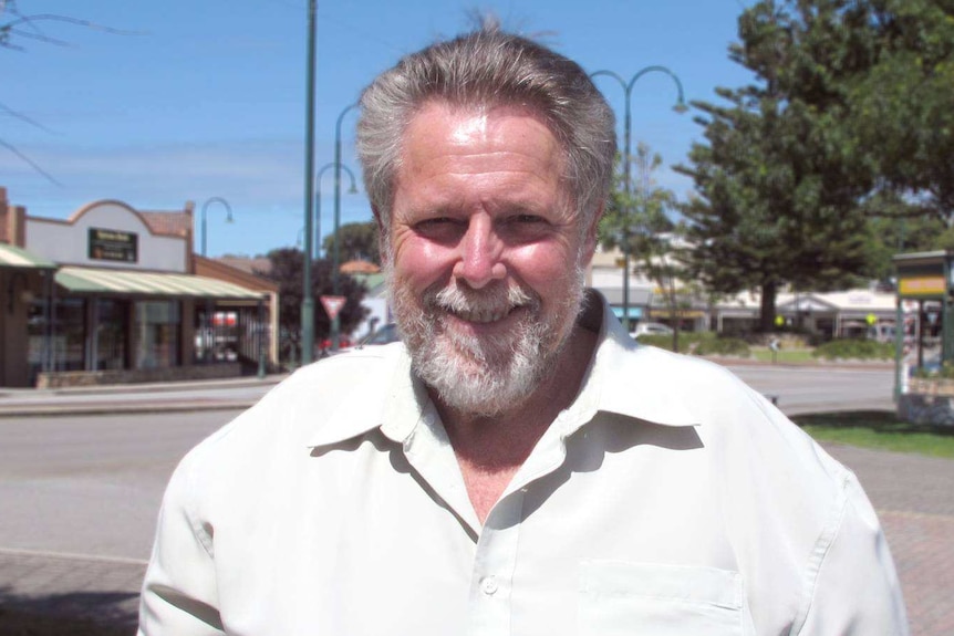 A man in a pal coloured shirt standing and smiling at the camera in the Albany CBD.