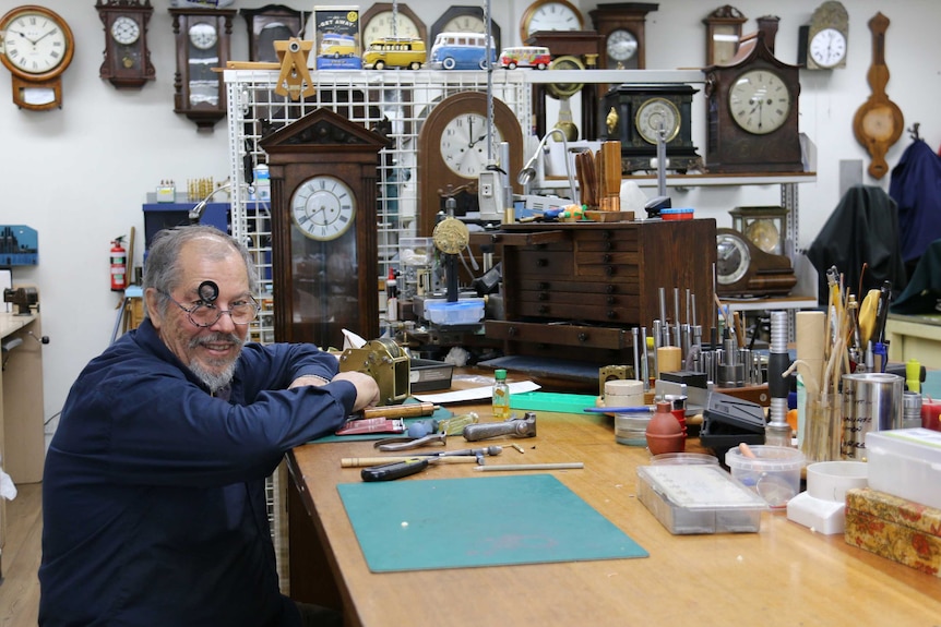 A man sits in a workshop of clocks.