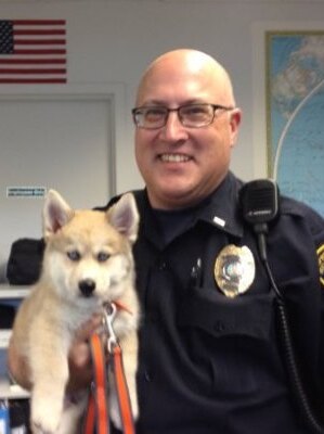 A photo of Jeff Neville in his police outfit while holding a dog.
