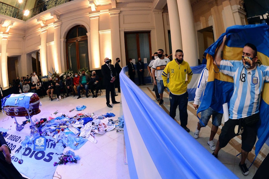 Fans with flags and wearing jerseys walk past Diego Maradona's coffin in the presidential palace in Buenos Aires, Argentina.