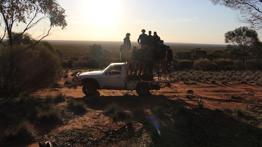 A white ute is parked in the bush with a group of teenage boys standing on the tray 