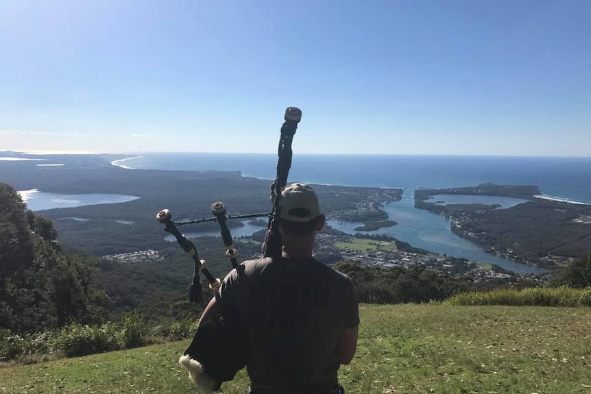 Keith Robinson standing on mountaintop playing the bagpipes looking out over the Hastings River in Port Macquarie.