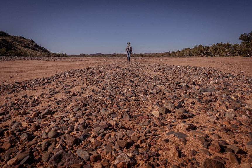 A man stands at the end of a long row of rocks.
