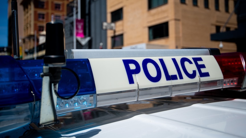 The top of a police car with the word 'Police' on it. Some city buildings are in the background