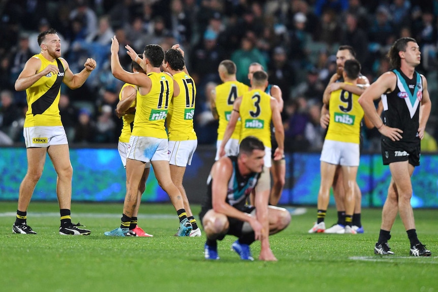 Port Adelaide players in the foreground are upset as a bunch of Richmond players celebrate behind them