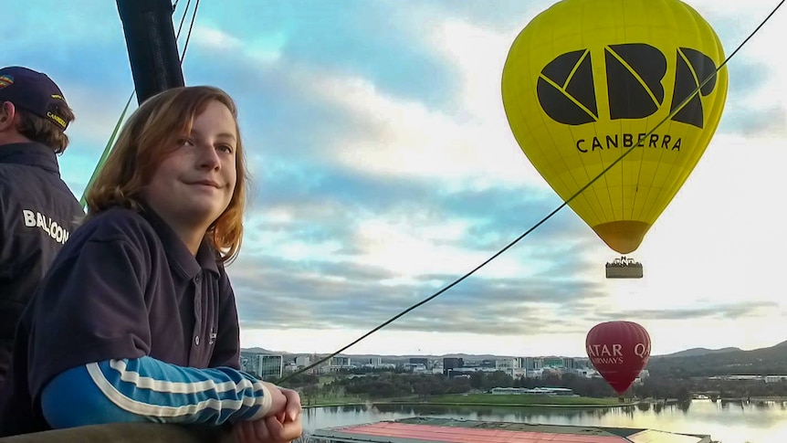 Boy smiling while leaning on edge of hot air balloon basket. 