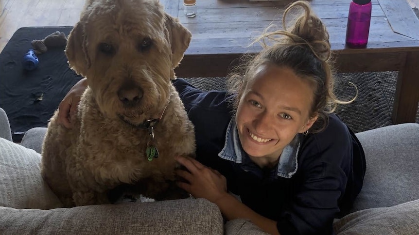 A young woman lies on a couch with her dog.