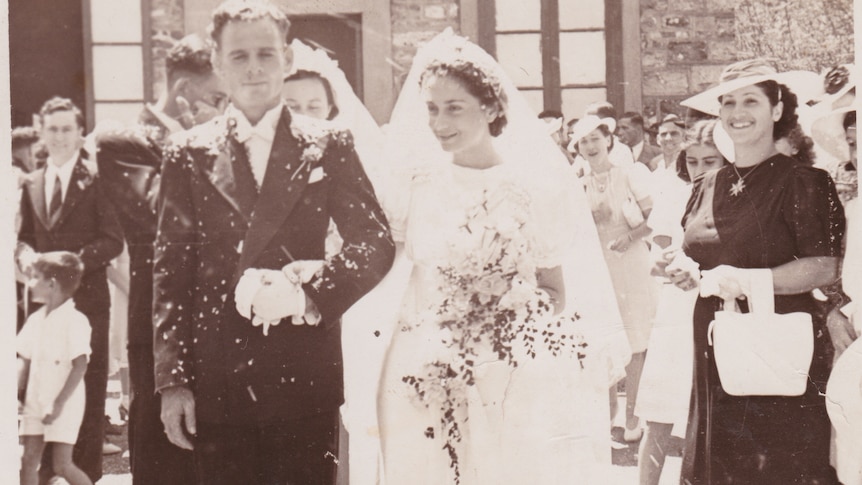 A 1940s sepia photo of a wedding, with a bride and groom outdoors, as others watch on