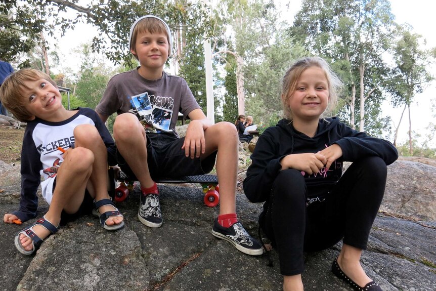 Three children - two boys and a girl - sit on a rock, smiling