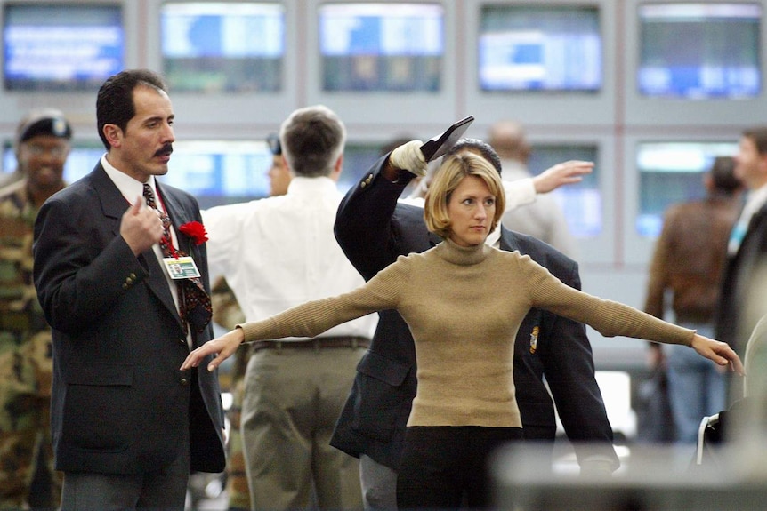 A security screener passes a metal-detecting wand over the head of a female traveller at an airport.