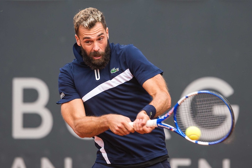 Benoit Paire opens his mouth and plays a two-handed back hand shot wearing a dark blue polo shirt