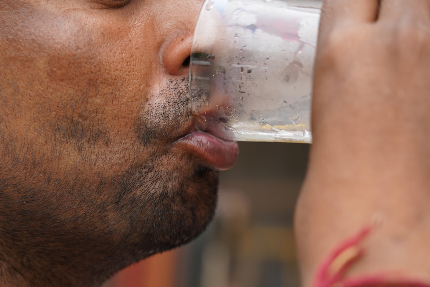 An Indian man holds a foggy water glass to his lips