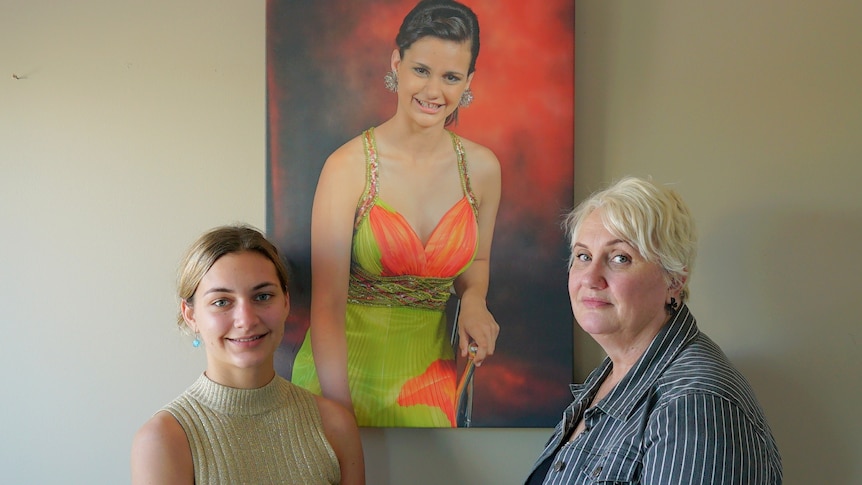 A teenage girl and her mother stand in front of a painted portrait of a young woman in a formal dress