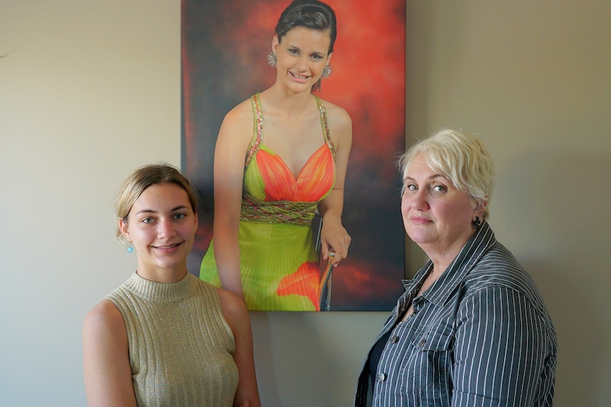 A teenage girl and her mother stand in front of a painted portrait of a young woman in a formal dress