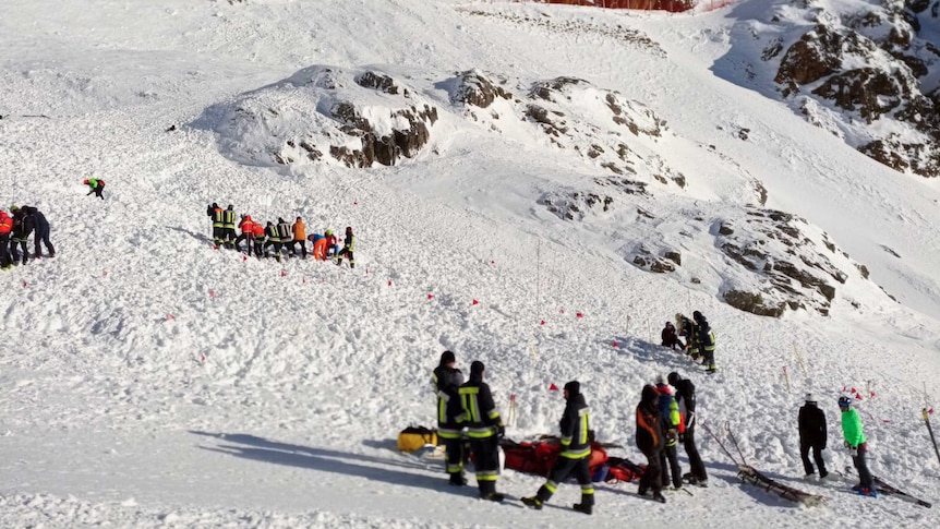 Groups of people in bright ski gear gathered at the base of a snowy mountain.
