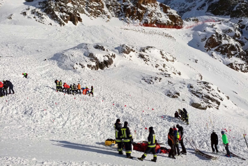 Groups of people in bright ski gear gathered at the base of a snowy mountain.