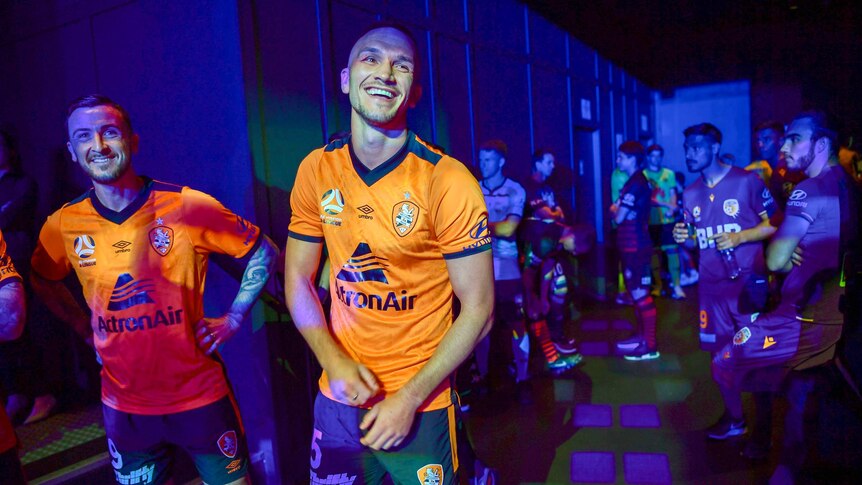 Two men in bright orange jerseys stand backstage.