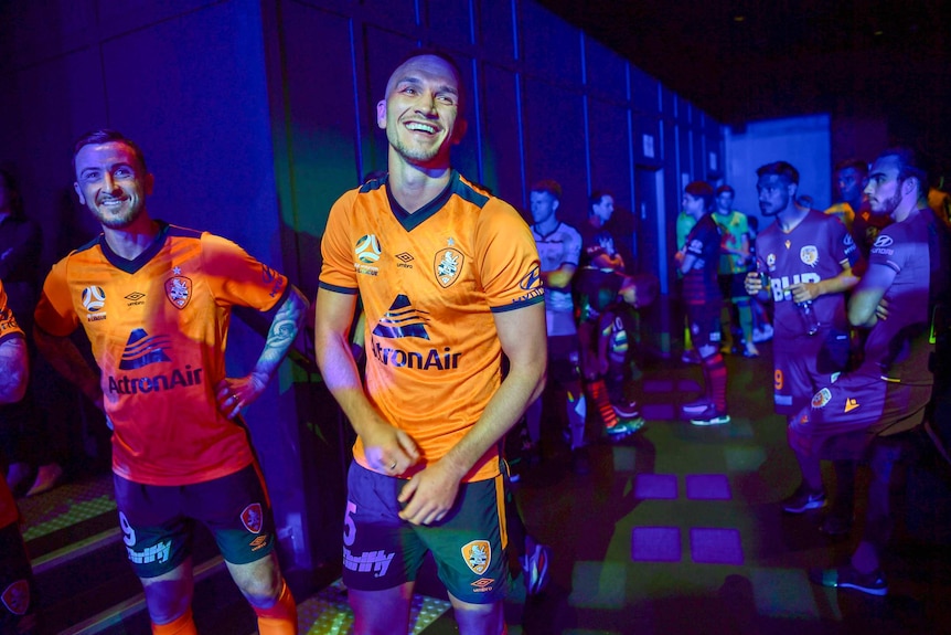 Two men in bright orange jerseys stand backstage.